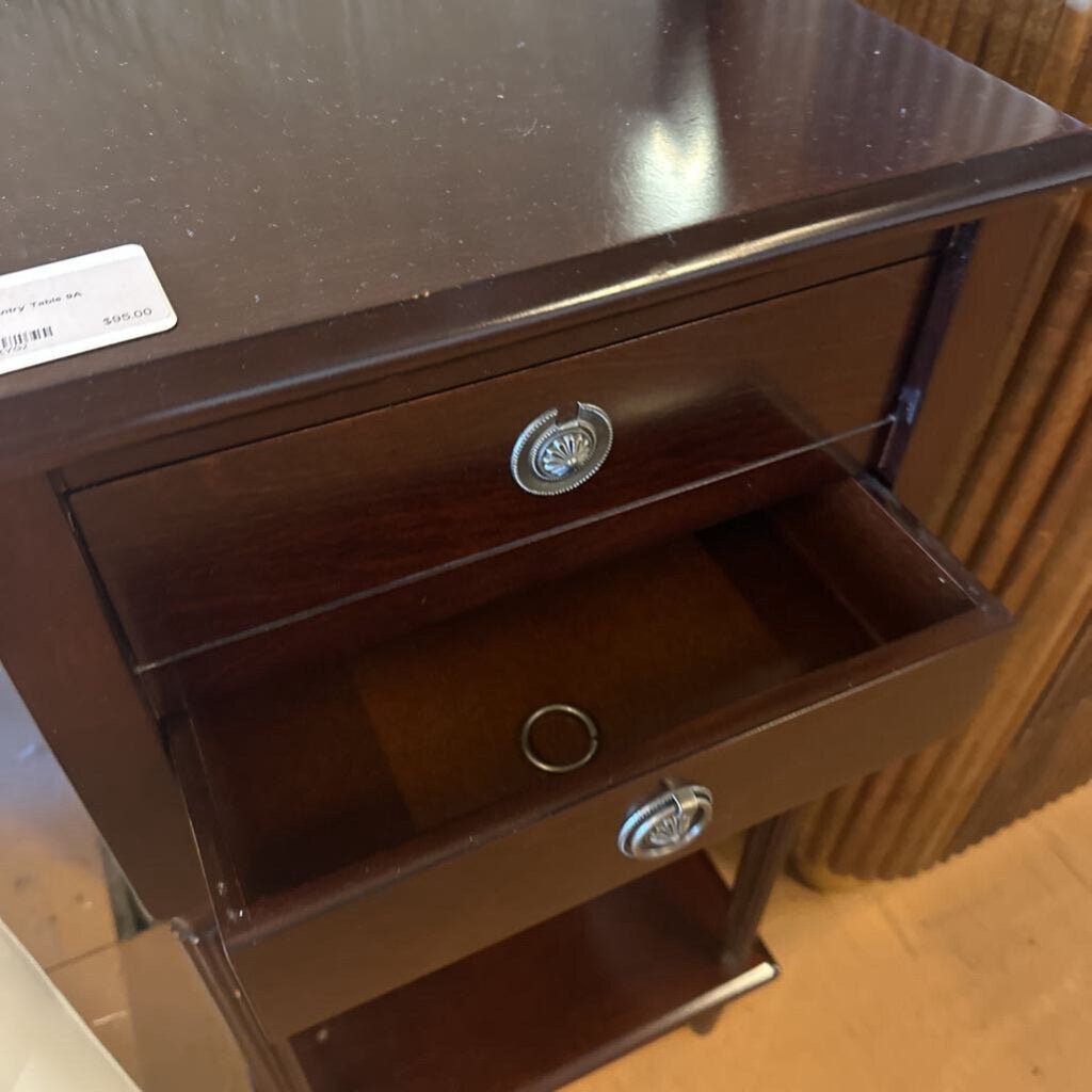 Wooden nightstand with two drawers and a metal handle on a wooden floor.