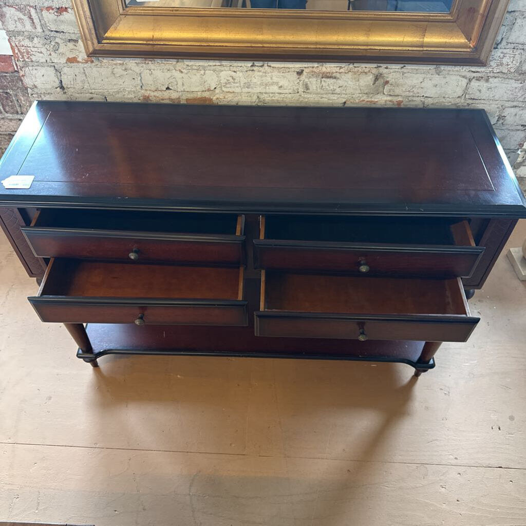 Wooden dresser with multiple drawers in a room with brick walls and a wooden floor.