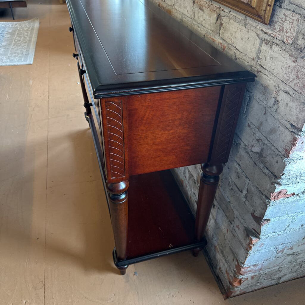 Wooden desk with a black top against a brick wall.