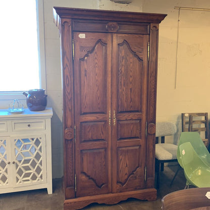 Wooden armoire in a room with chairs and a window.