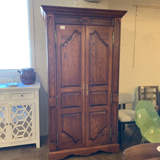 Wooden armoire in a room with chairs and a window.