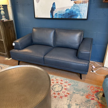 Blue leather sofa in a room with a colorful rug and abstract painting on the wall.
