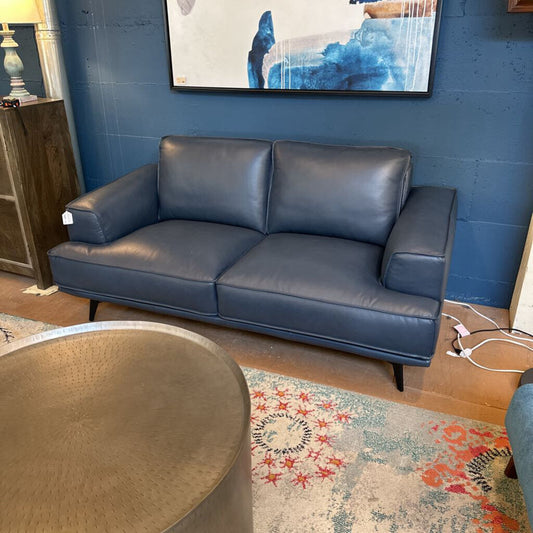 Blue leather sofa in a room with a colorful rug and abstract painting on the wall.