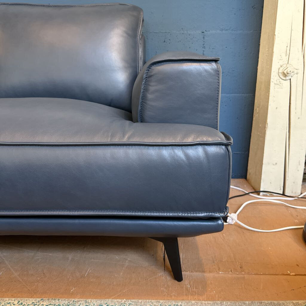 Blue leather sofa against a blue wall with a wooden floor.