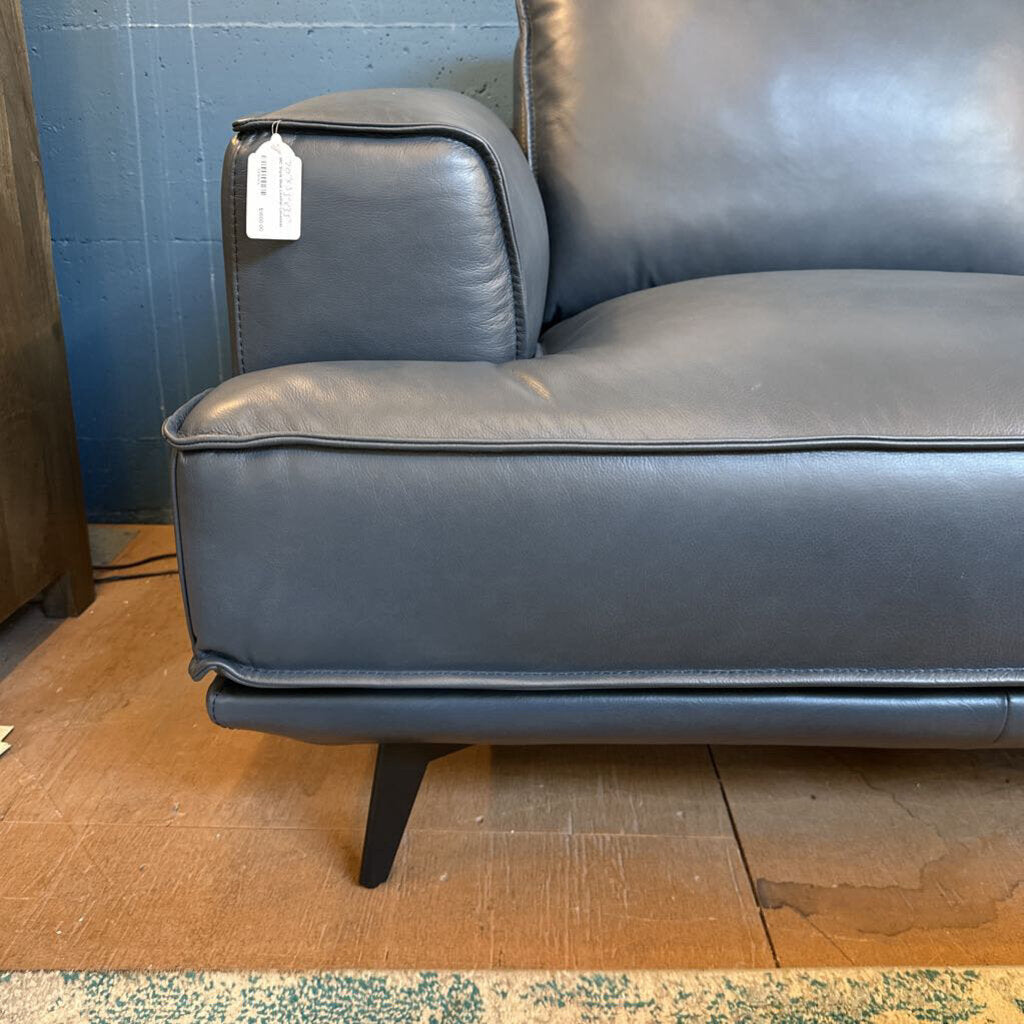 Gray leather sofa with a tag on a wooden floor against a blue wall.