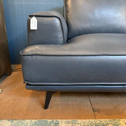 Gray leather sofa with a tag on a wooden floor against a blue wall.