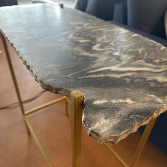 Table with a stone-like top and gold metal legs on a wooden floor.