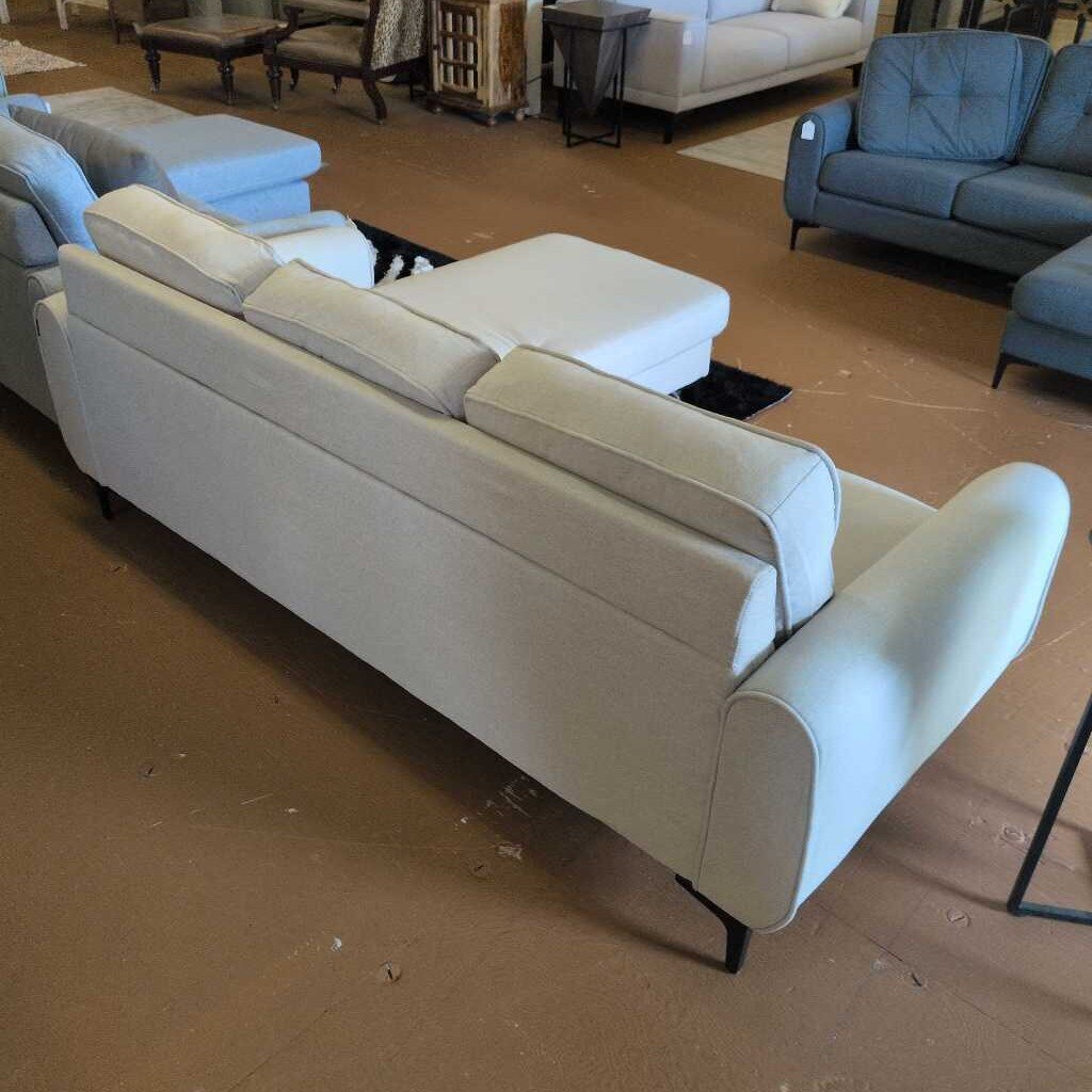 Beige sectional sofa in a showroom setting with other furniture.