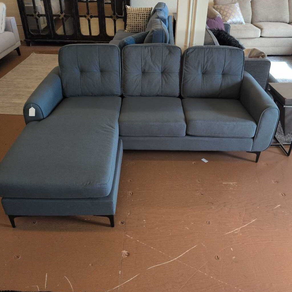 Gray sectional sofa on a brown floor with a blurred background