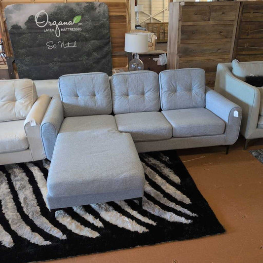 Gray sectional sofa with ottoman on a black and white patterned rug, with 'Organa' branding in the background.