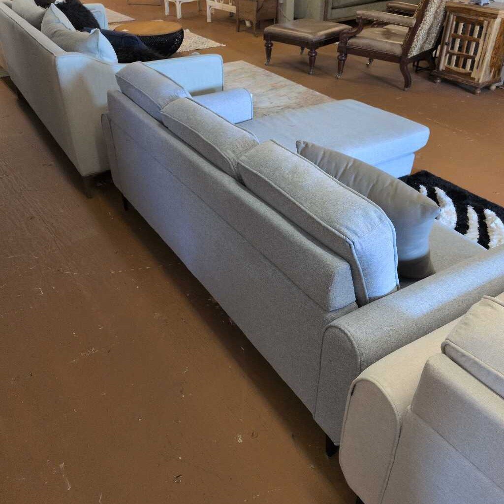 Gray sectional sofa in a room with wooden flooring and furniture.
