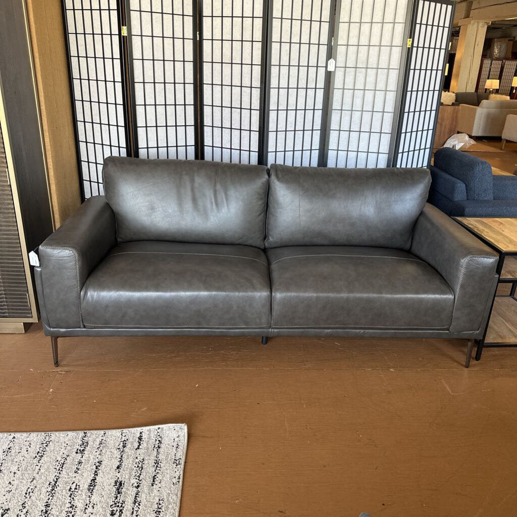 Gray leather sofa in a room with a black screen wall and wooden floor.