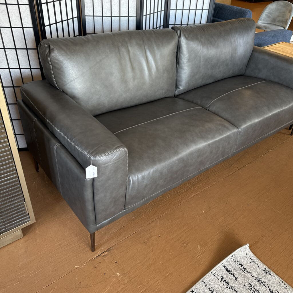 Gray leather sofa in a room with wooden flooring and a black and white patterned wall.