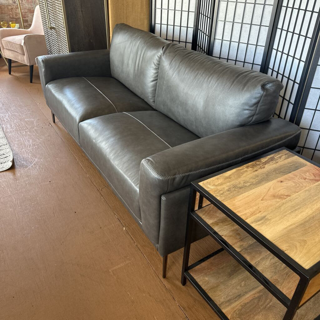 Gray leather sofa in a room with wooden flooring and a small table.