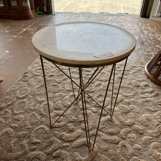 Round marble table with metal legs on a textured stone floor
