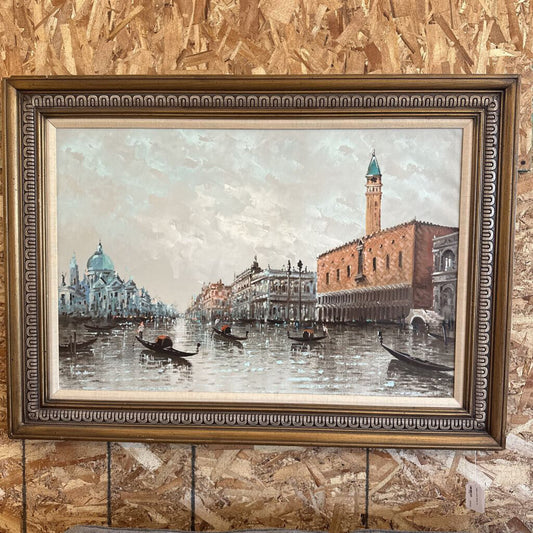 Framed painting of a cityscape with boats and buildings on a textured wall.