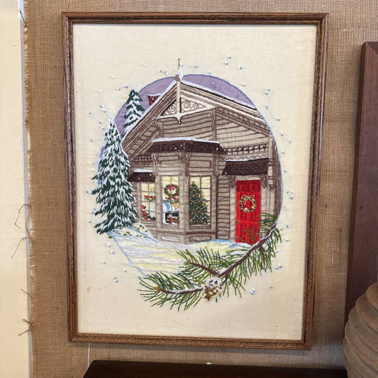 Framed embroidered picture of a house with a red door and Christmas decorations, on a textured beige background.