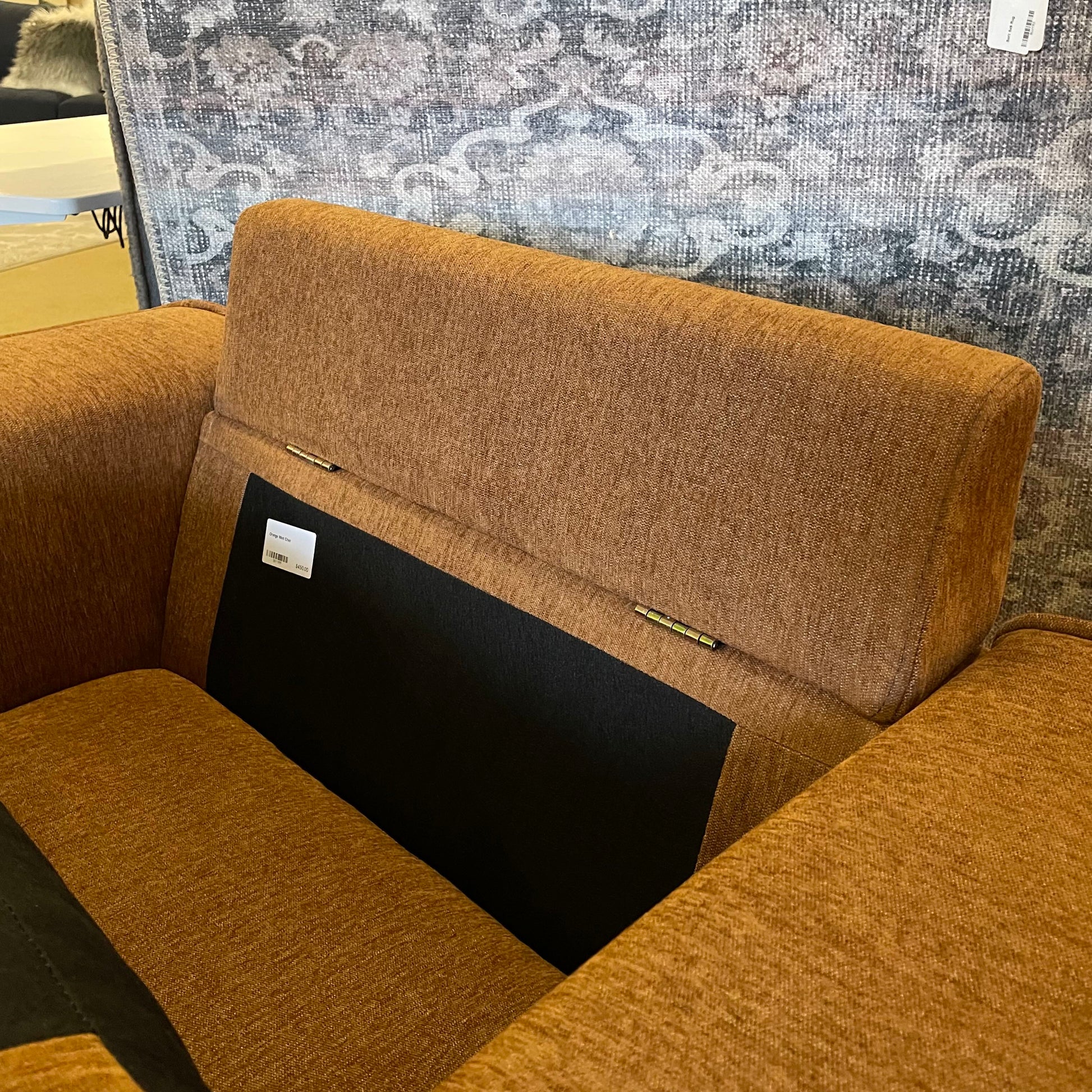 Brown upholstered chair with a black cushion against a textured wall.