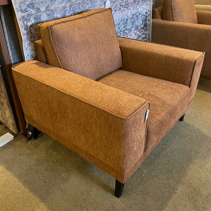 Brown armchair with a visible tag on a carpeted floor