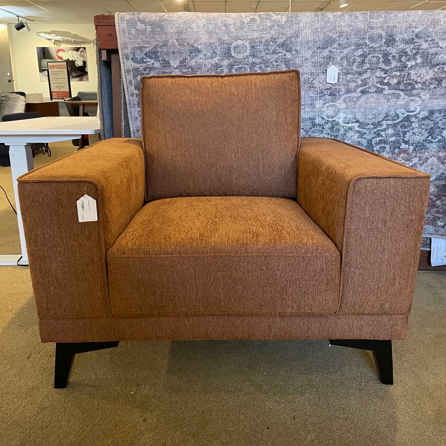 Brown armchair in a showroom setting with a patterned rug in the background.