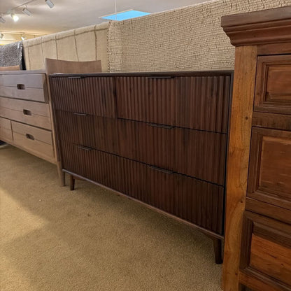 Wooden dresser with a textured wall and carpeted floor in the background