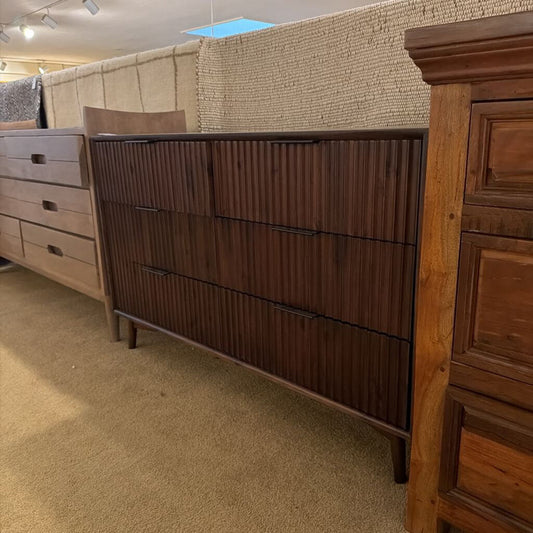 Wooden dresser with a textured wall and carpeted floor in the background
