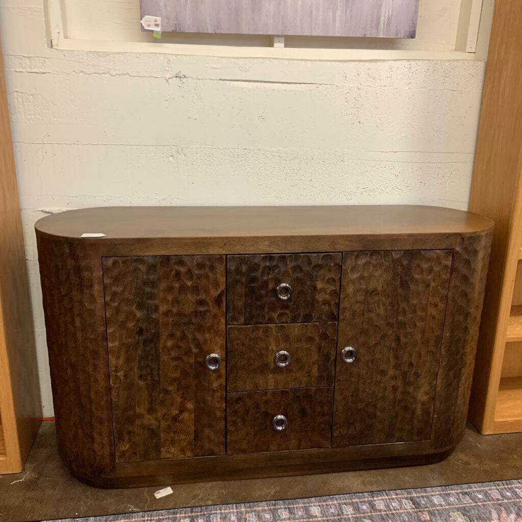 Wooden sideboard with a textured finish against a white brick wall.