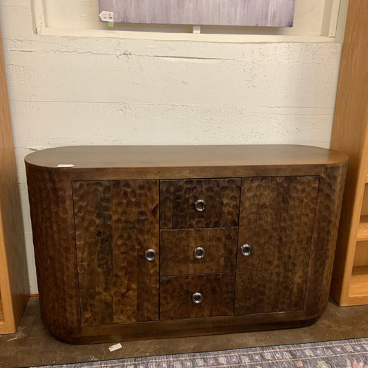 Wooden sideboard with a textured finish against a white brick wall.