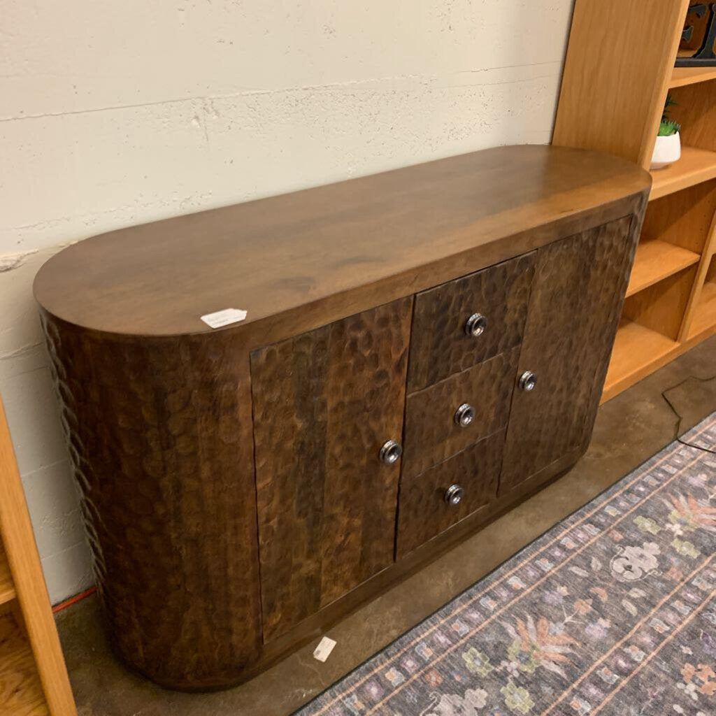 Wooden sideboard with three doors against a white brick wall.