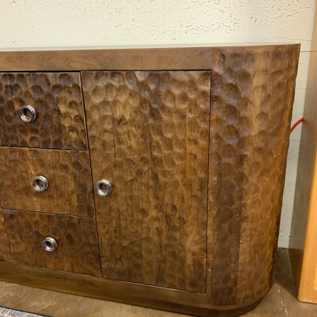Wooden cabinet with hammered texture and metallic knobs against a plain wall.