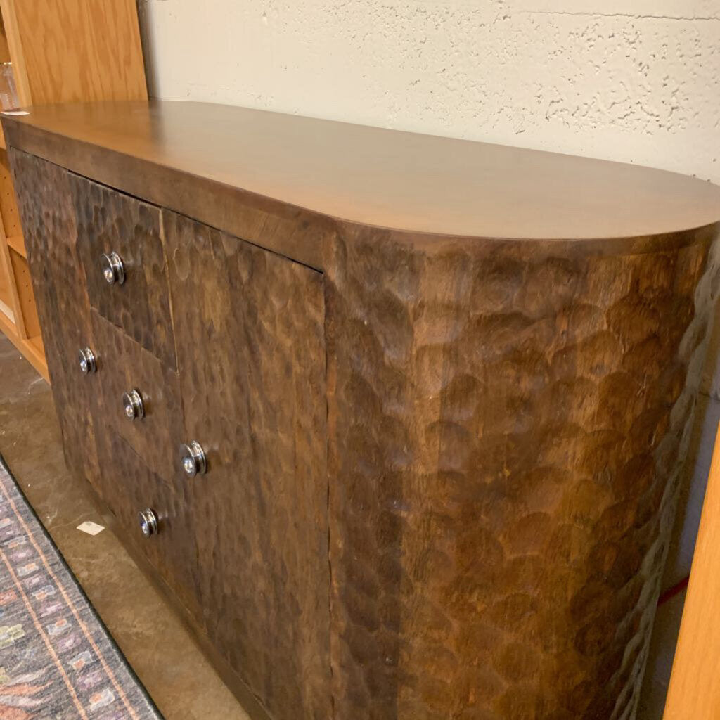 Wooden sideboard with a textured finish and metallic knobs against a neutral wall.