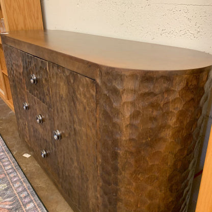 Wooden sideboard with a textured finish and metallic knobs against a neutral wall.