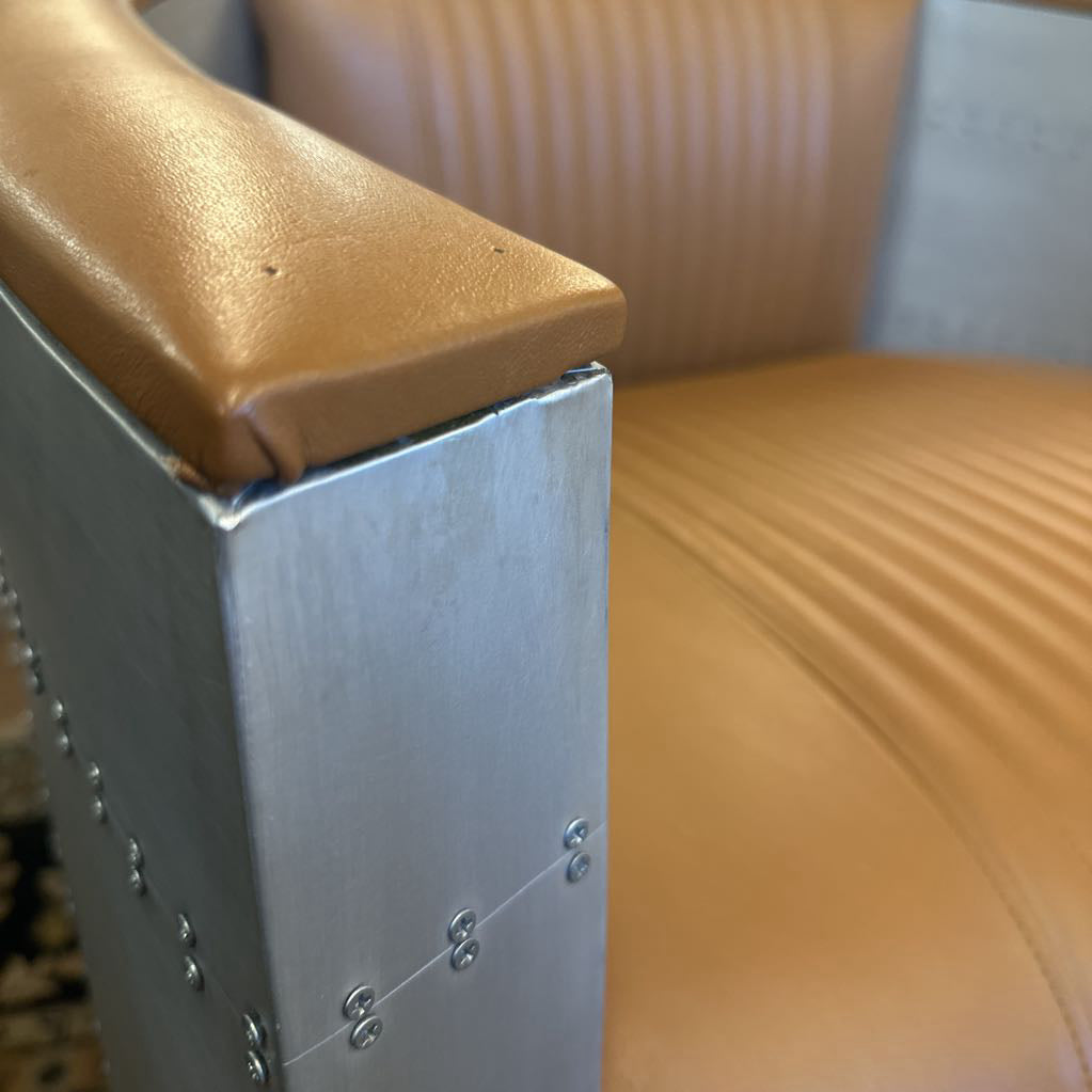 Close-up of a brown leather chair with metal armrests.