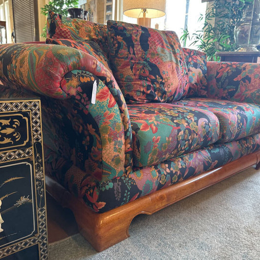 Multicolored floral-patterned sofa with wooden legs in a room setting.