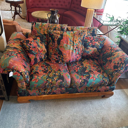 Multicolored floral-patterned sofa in a living room setting with a red couch and lamp in the background.