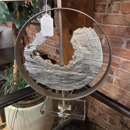 Decorative metal piece with a textured surface on a stand against a brick wall.