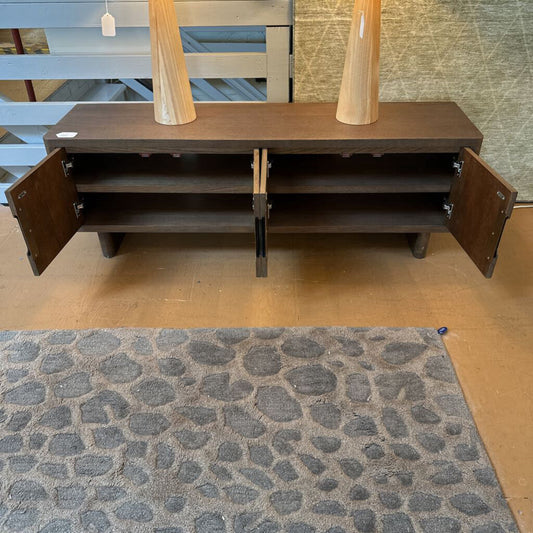 Wooden sideboard with open doors on a wooden floor with a textured rug.