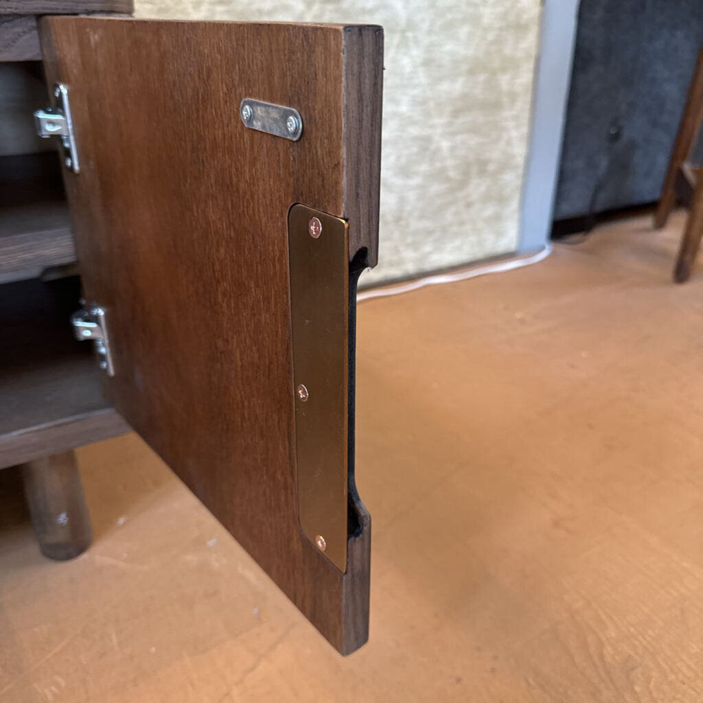 Close-up of a wooden cabinet door with a metal hinge on a wooden floor.