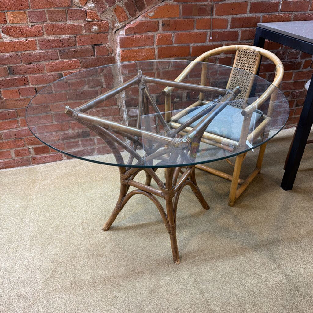 Round glass table with wicker chair against a brick wall.