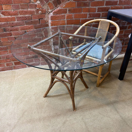 Round glass table with wicker chair against a brick wall.