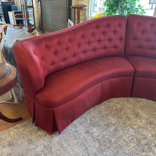 Red curved sofa in a room with a rug and furniture.