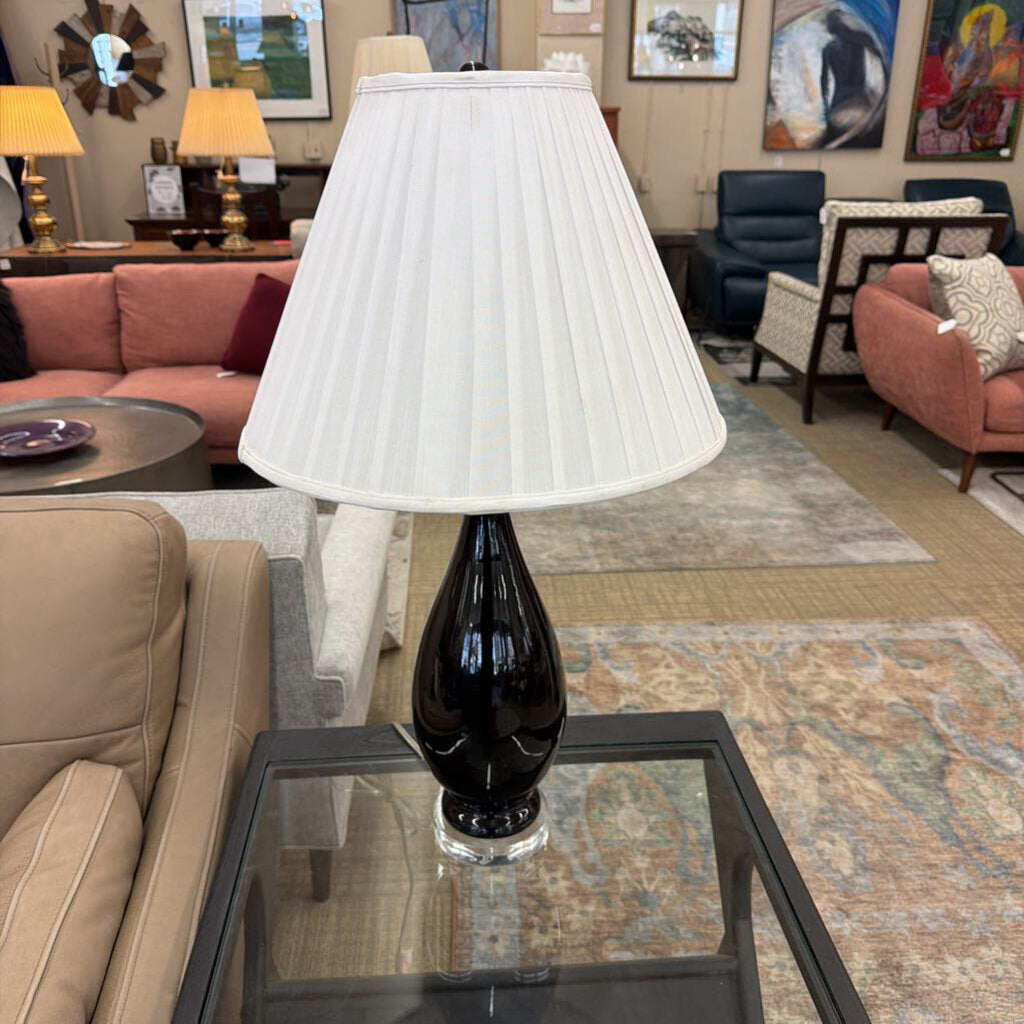 Black lamp with a white shade on a glass table in a living room setting.