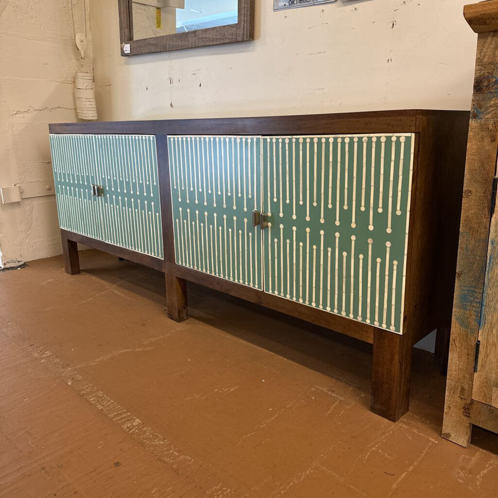 Wooden sideboard with green and white patterned doors in a room setting.