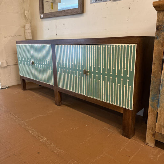 Wooden sideboard with green and white patterned doors in a room setting.