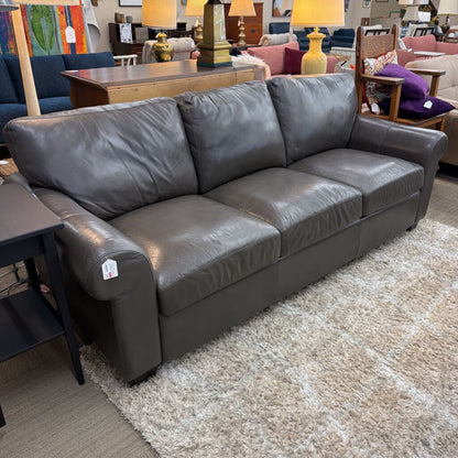 Gray leather sofa in a furniture store setting with various other items in the background.
