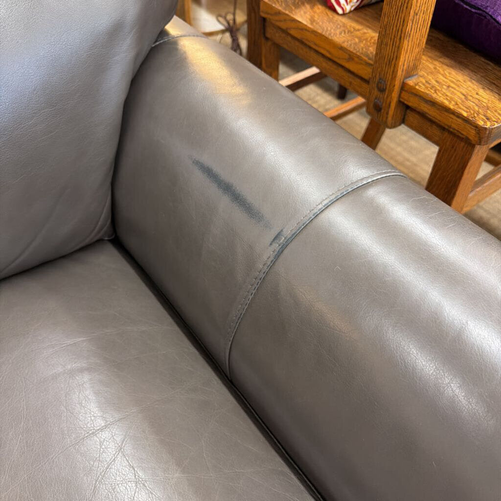 Gray leather sofa with a noticeable scratch on the armrest, wooden chair in the background.