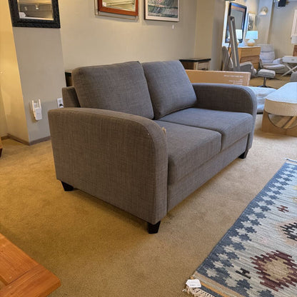 Gray sofa in a showroom setting with other furniture and decor items.