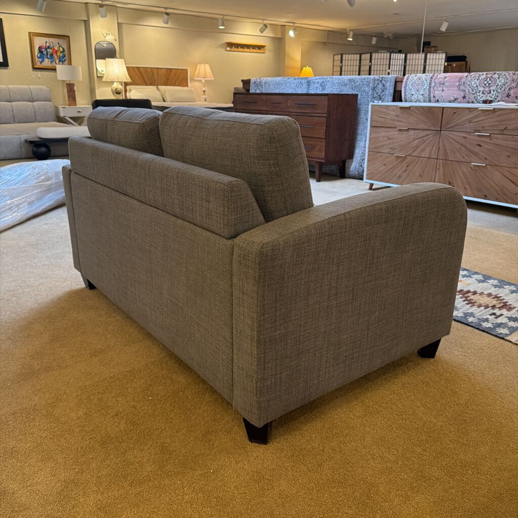 Brown sofa in a furniture store with various other furniture pieces in the background.