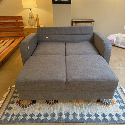 Gray sectional sofa in a living room setting with a rug and wooden furniture.