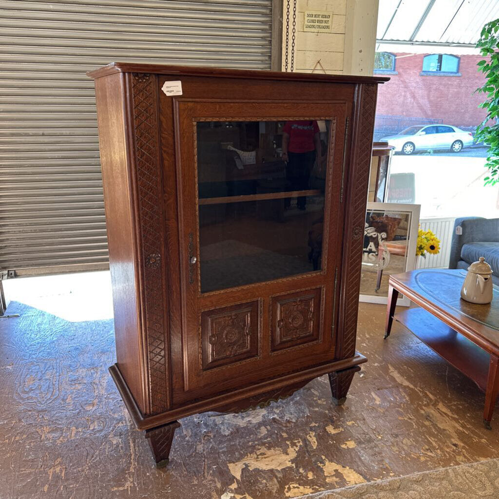 Wooden cabinet with glass door in a room with a couch and table.